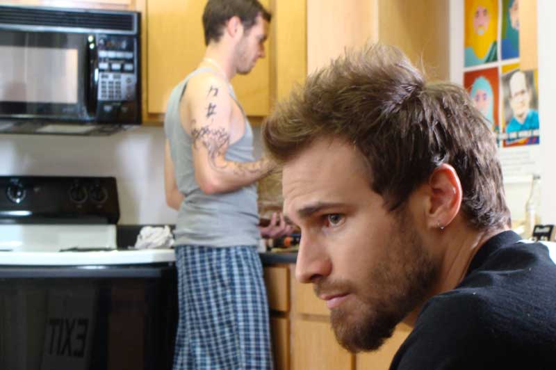 Man sits in kitchen while roommate cooks