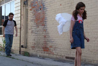 Man follows young girl wearing angel wings down a dingy alley